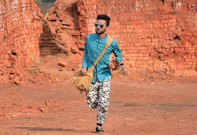 a man running with a crossbody bag wearing camouflage pants and a blue shirt