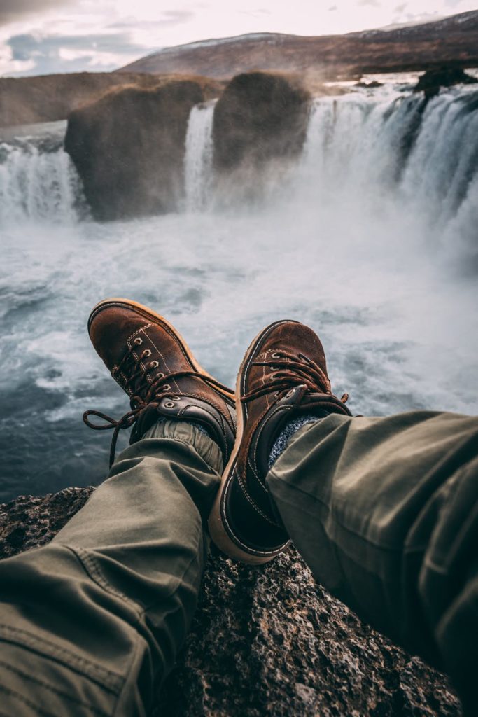 a man sitting on a cliffside wearing cargo pants and boots