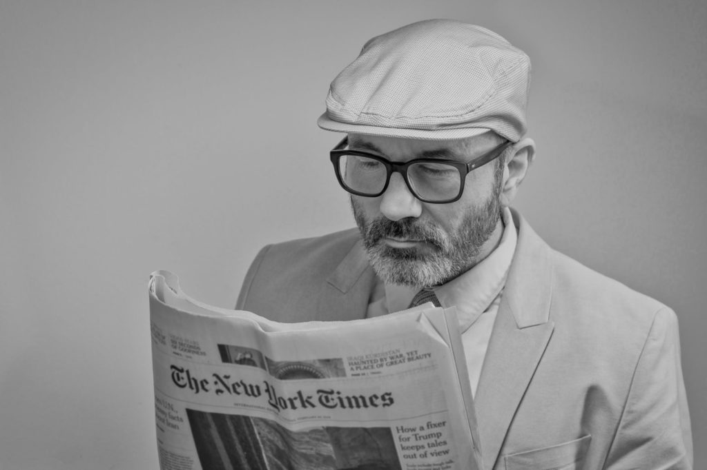 a man wearing a kangol cap with black glasses reading the newspaper