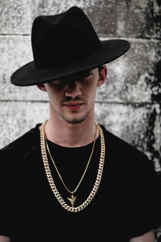 a man wearing black clothes with a black hat and gold chain necklaces
