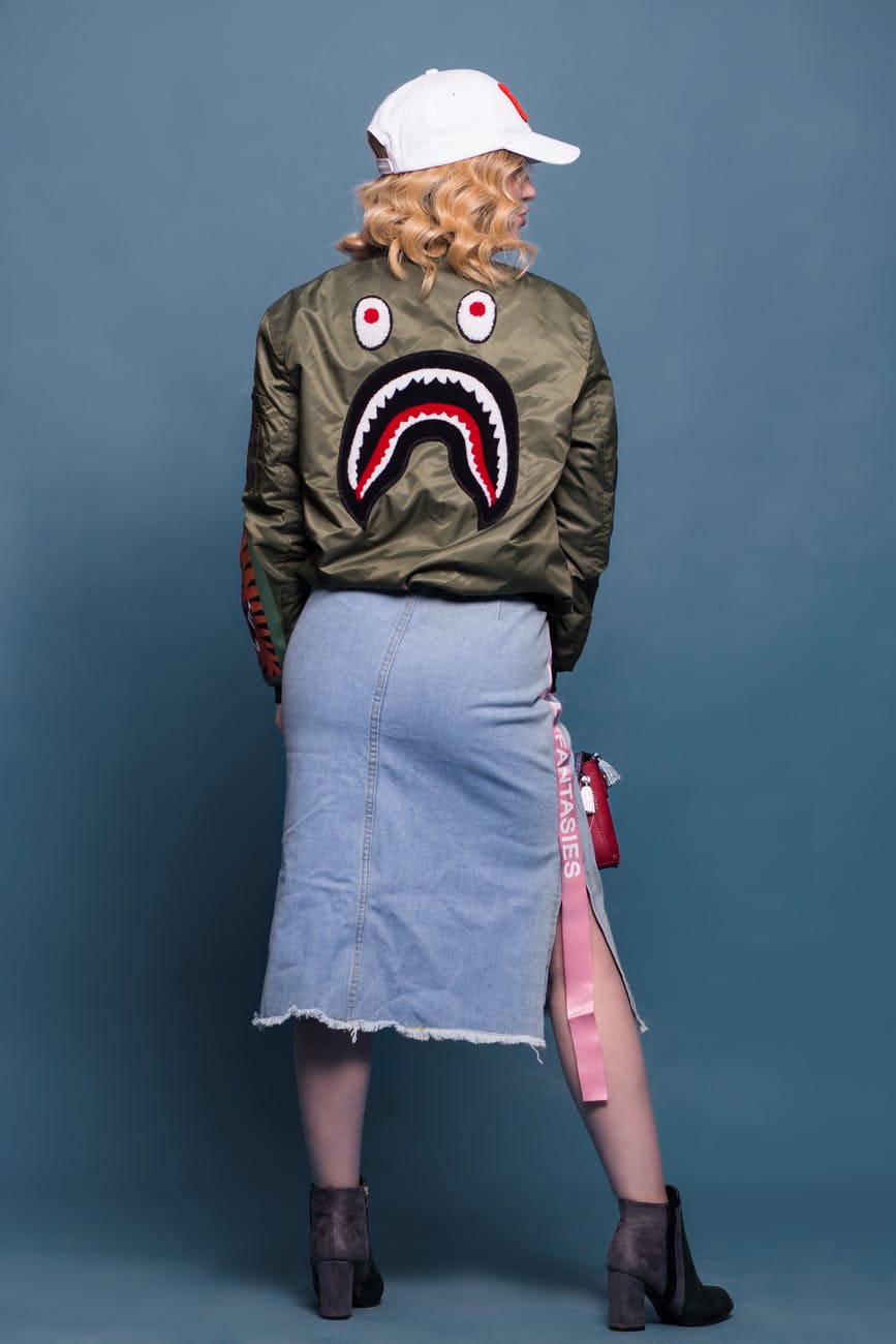 a woman wearing a bomber jacket with a denim skirt
