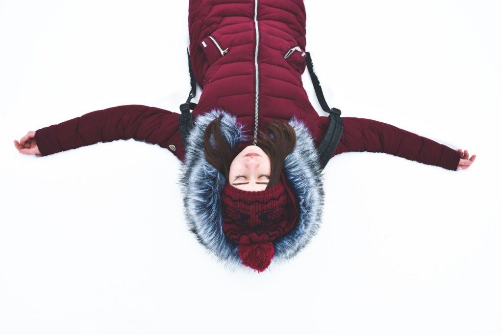 a woman wearing a parka and lying down in the snow