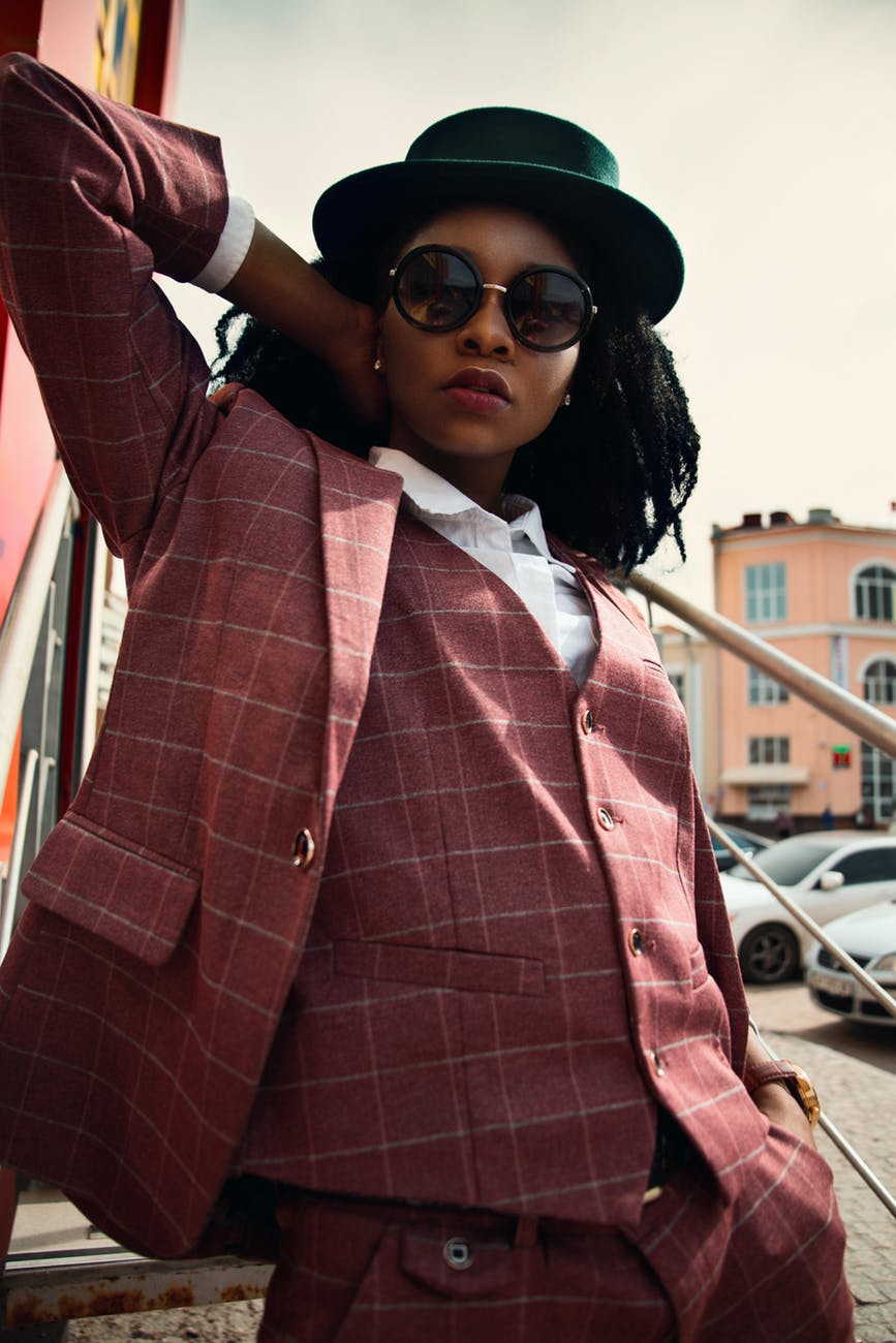 a woman wearing maroon men’s suit with sunglasses and a bowler hat