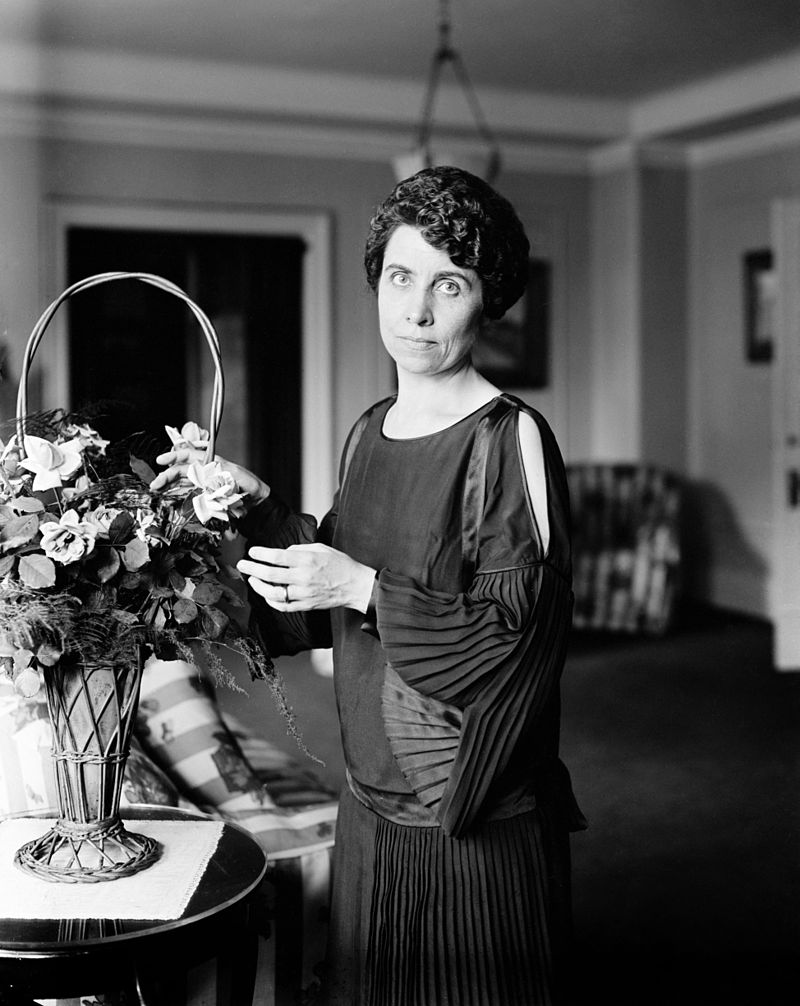 Grace Coolidge, wife of Calvin Coolidge, standing next to a flower vase