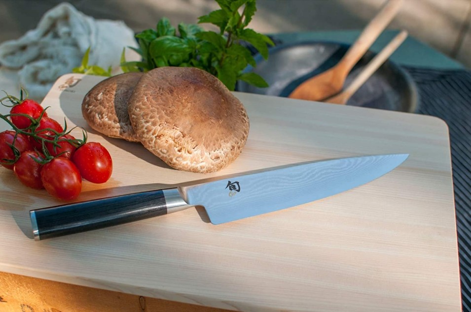 a chef’s knife on a wooden cutting board along with bread and cherry tomatoes