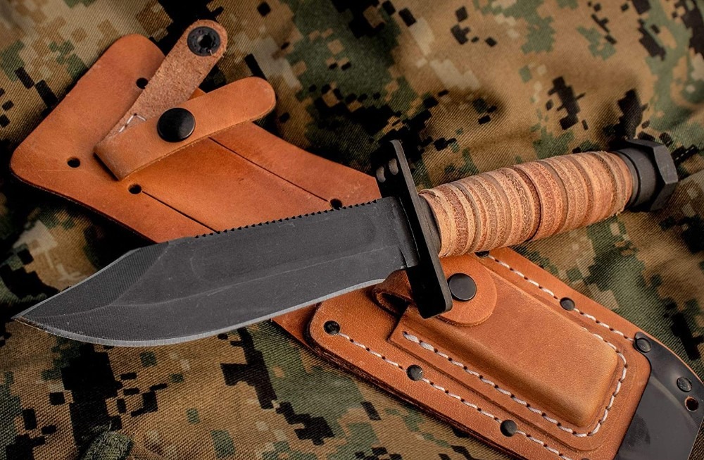a survival knife having a black blade and brown handle on top of a leather sheath