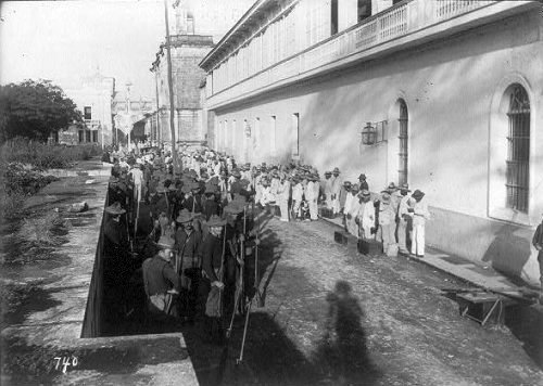1899: U.S. soldiers and Filipino POWs gather on Postigo Street near the Manila Cathedral, Intramuros district, Manila.