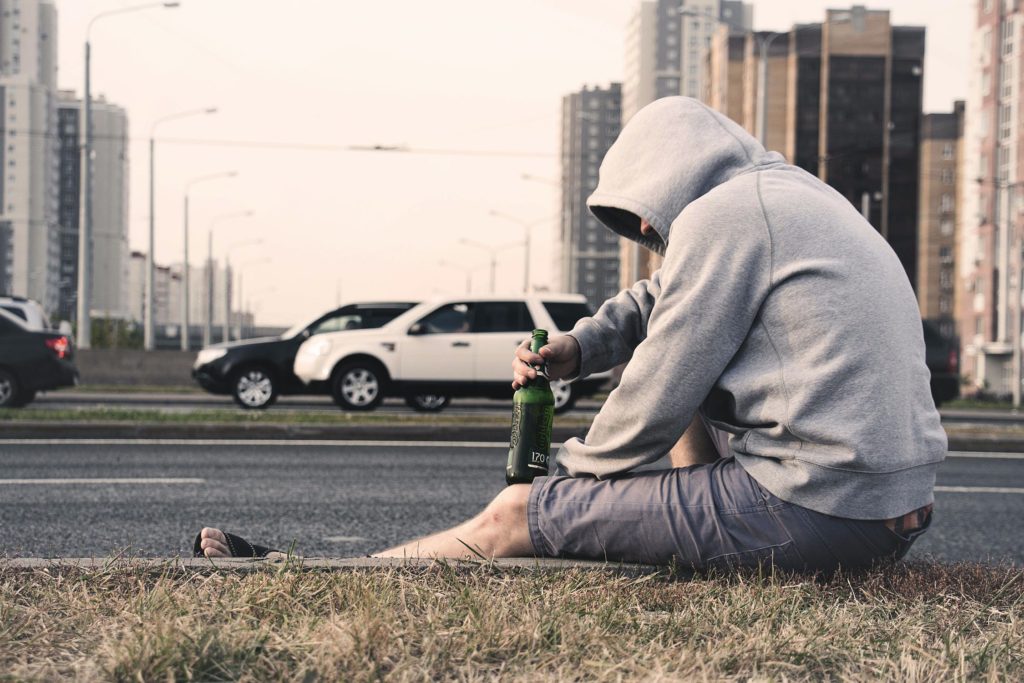 an alcoholic sitting on the side of the road 