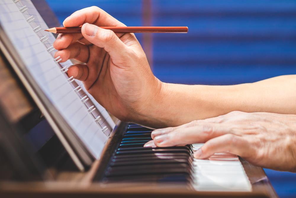 Musician hand writing a song while playing acoustic piano