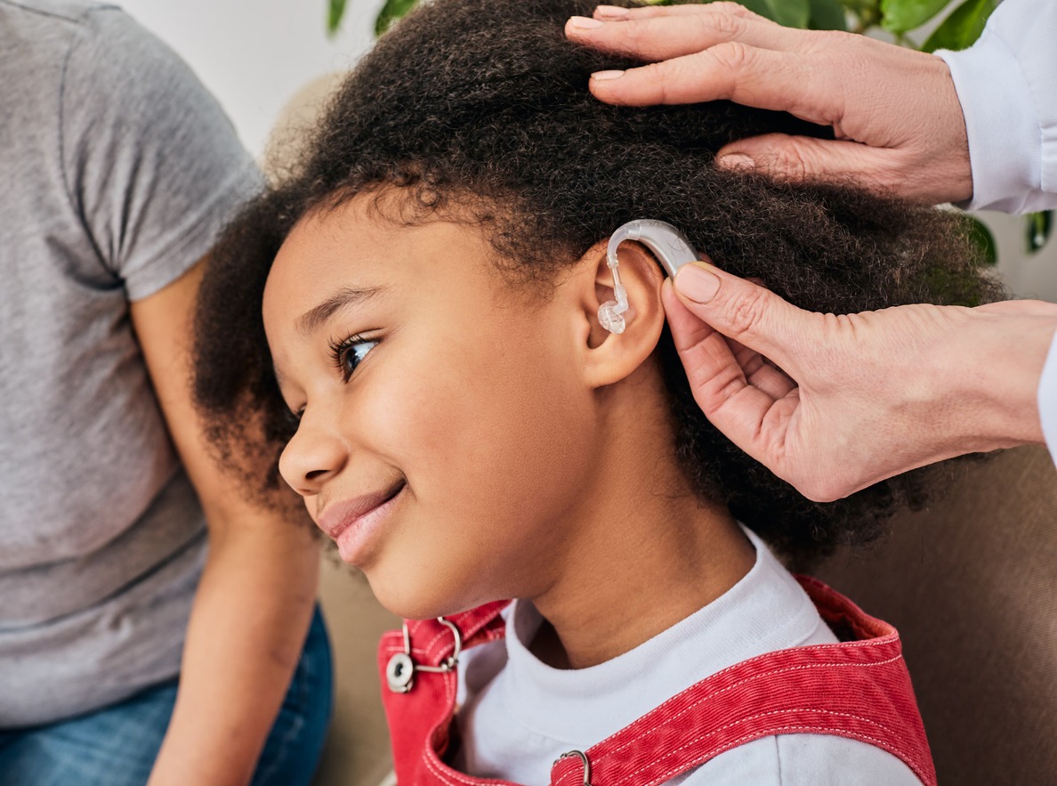 Hearing solutions for children. Doctor installs hearing aid on African American girl's ear, close-up