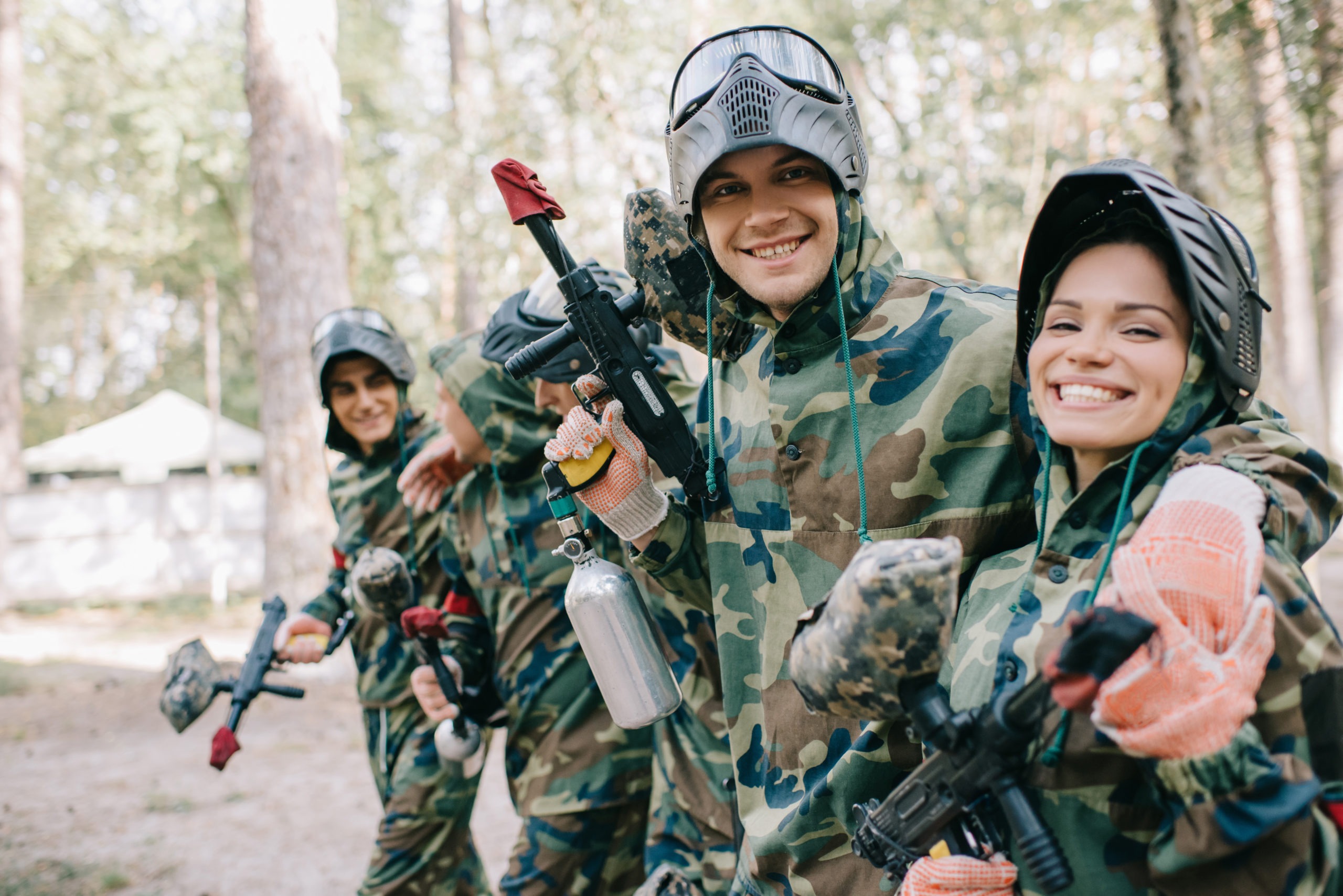 smiling young male paintballer embracing female teammate in camouflage with paintball gun outdoors