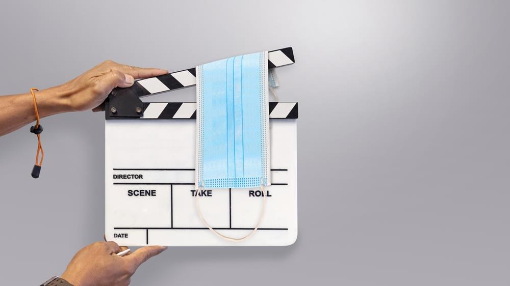 Man holding a movie clapperboard with a surgical mask