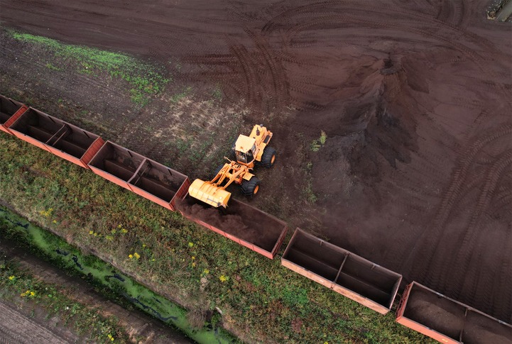 Wheel loader loads peat in freight cars. Aerial view of diesel locomotive on railroad in landscape at wetlands.