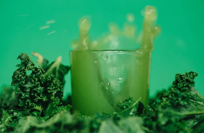 bright vitamin juice near lettuce leaves on green background