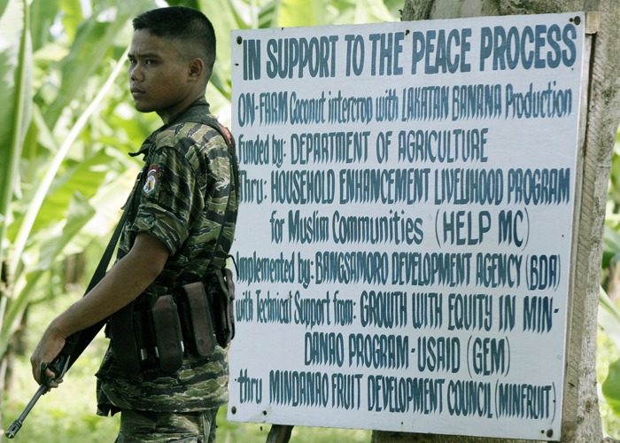 A Moro rebel standing in front of a sign describing an initiative by the USAID "Growth With Equity in Mindanao" farming program staged at the Moro Islamic Liberation Front (MILF) outpost inside the MILF Camp at Darapanan in Sultan Kudarat, Southern Philippines. (2008)