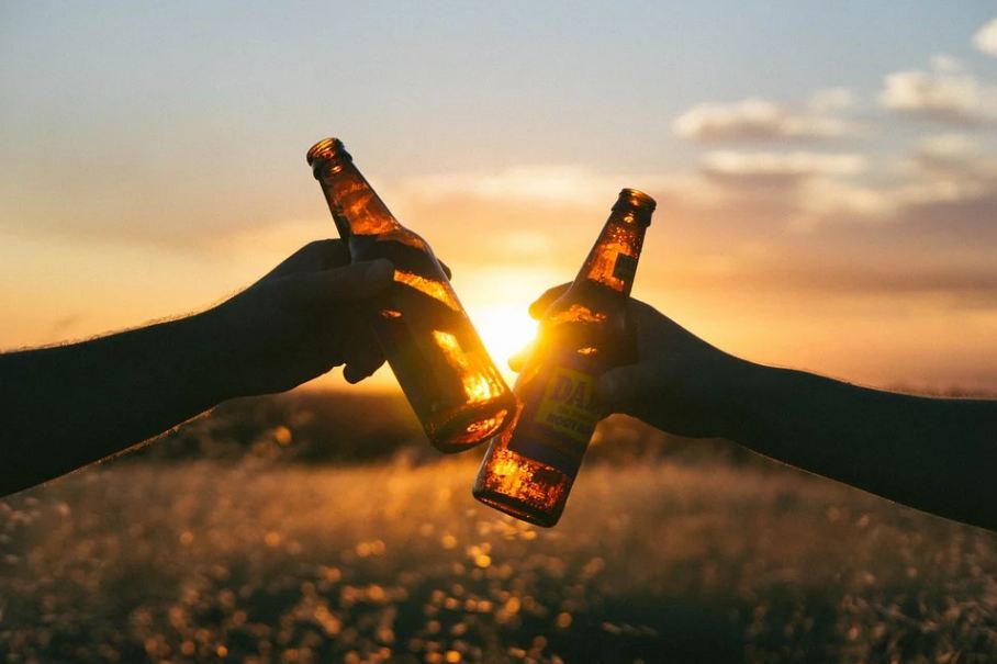 two-hands-holding-a-beer-bottle-against-the-sunset