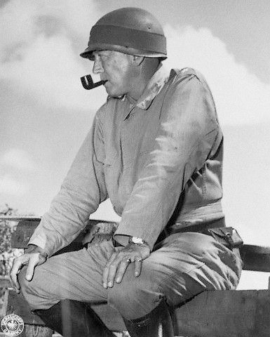 Lieutenant General George S. Patton sitting on a fence and smoking a pipe