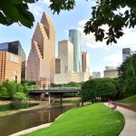 Wide shot of Houston's modern skyline and paved bicycle/walking path in Buffalo Bayou Park on a summer afternoon